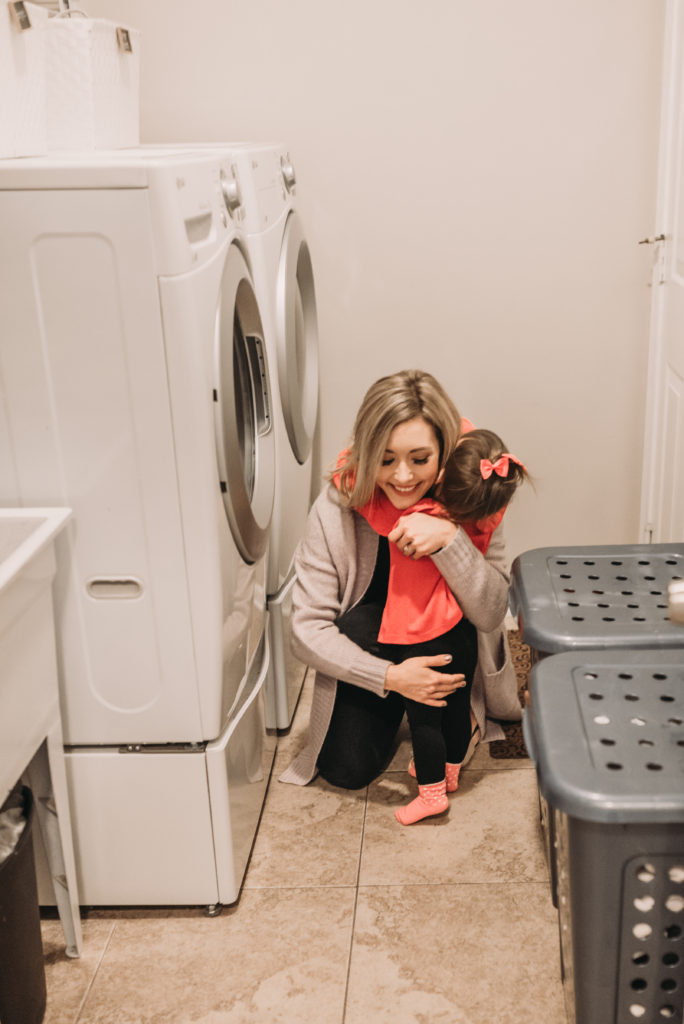  Brianna K in her laundry room hugging Presley in front of her washer and dryer after sharing 5 easy laundry hacks and tips! Bits of Bri blog laundry room tips and tricks 
