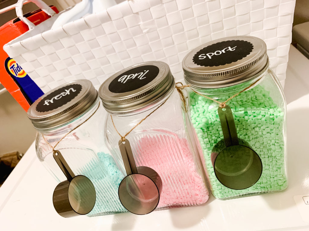 Scent booster crystals in mason jars on top of Brianna K's washing machine labeled with chalk labels.  Brianna K in her laundry room with children Landon and Presley giving a high five after sharing 5 easy laundry hacks and tips! Bits of Bri blog laundry room tips and tricks 