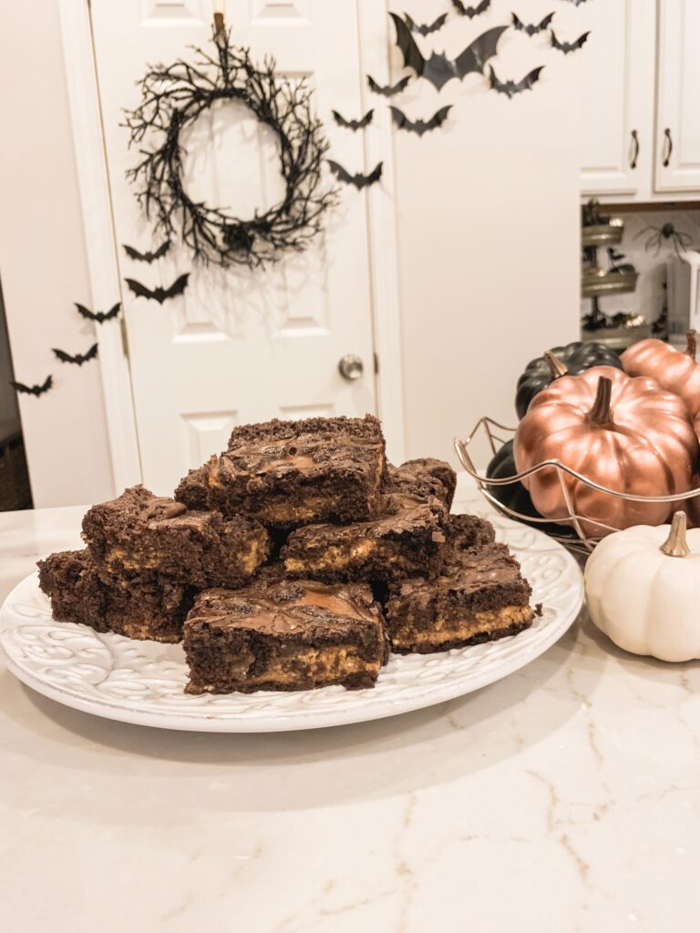 Platter of pumpkin swirl brownies on white plate with rose gold and black pumpkin home decor. Pumpkin swirl brownie recipe for fall baking 2019 Brianna K bitsofbri pumpkin swirl brownie pumpkin brownie recipe fall halloween thanksgiving brownie recipes ideas baking 