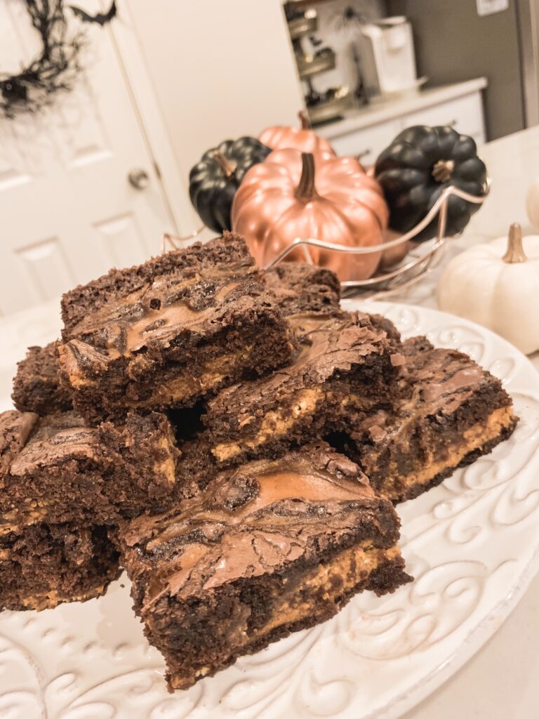 Platter of pumpkin swirl brownies on white plate with rose gold and black pumpkin home decor. Pumpkin swirl brownie recipe for fall baking 2019 Brianna K bitsofbri pumpkin swirl brownie pumpkin brownie recipe